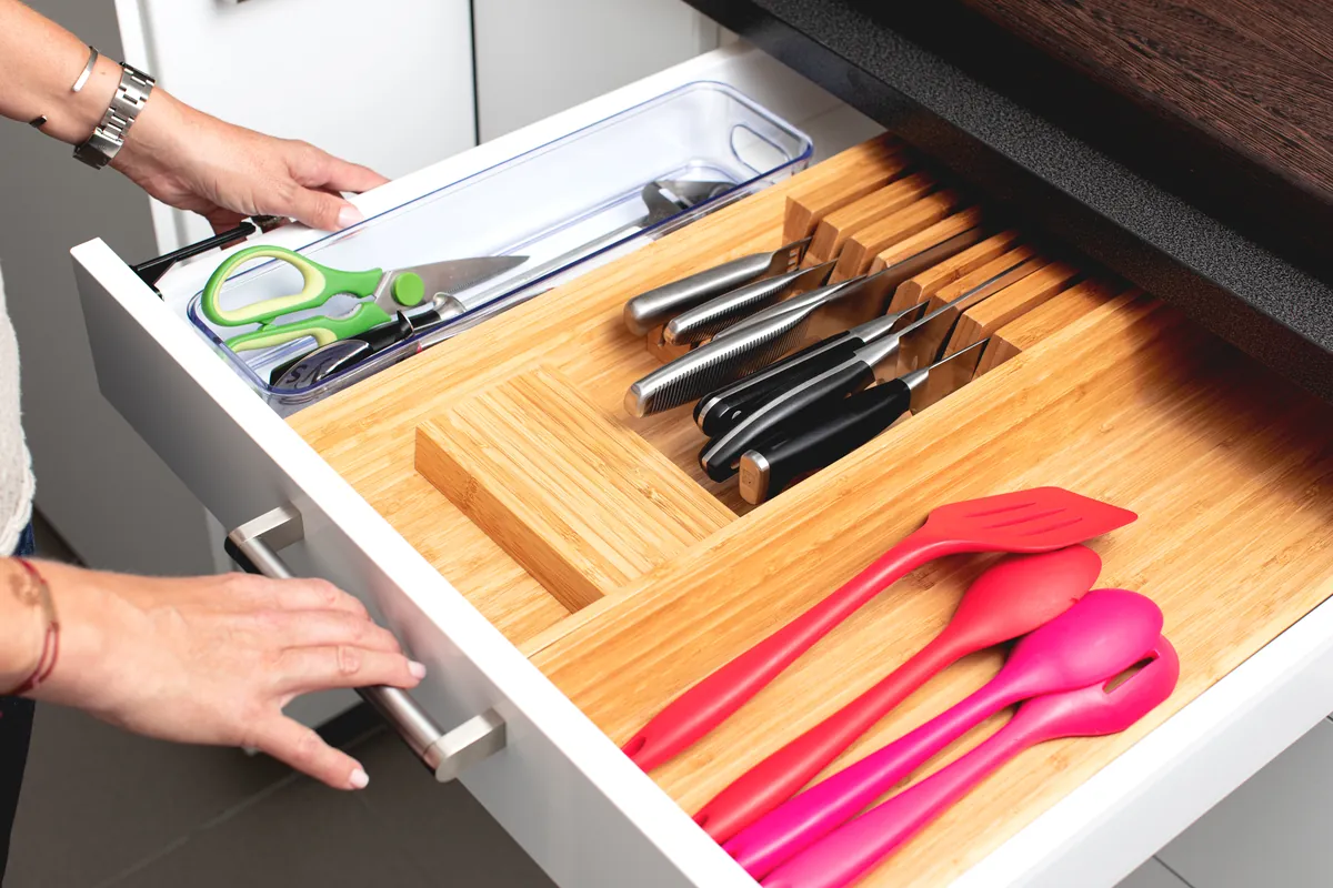 An open kitchen drawer with a bamboo organiser for knives and utensils