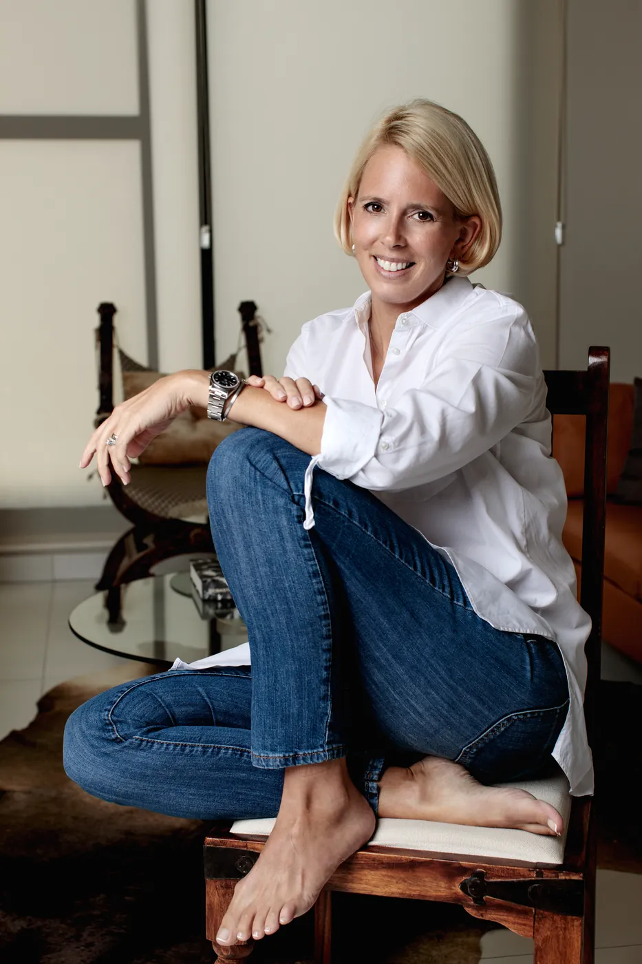 Wiebke Buelow at home, seated on a wooden chair in a white shirt and jeans